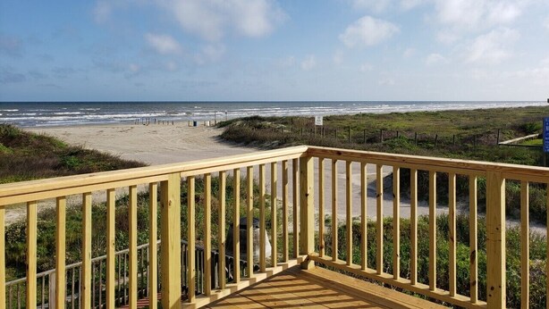 Eine Holzterrasse mit Blick auf einen Strand und einen klaren Himmel.