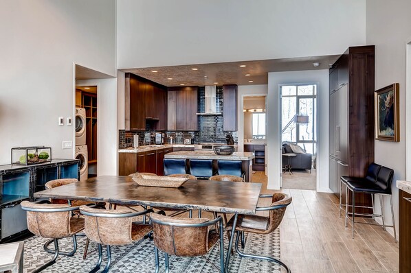 A modern kitchen with dark wood cabinets, a central island with seating, and a view to the living area.