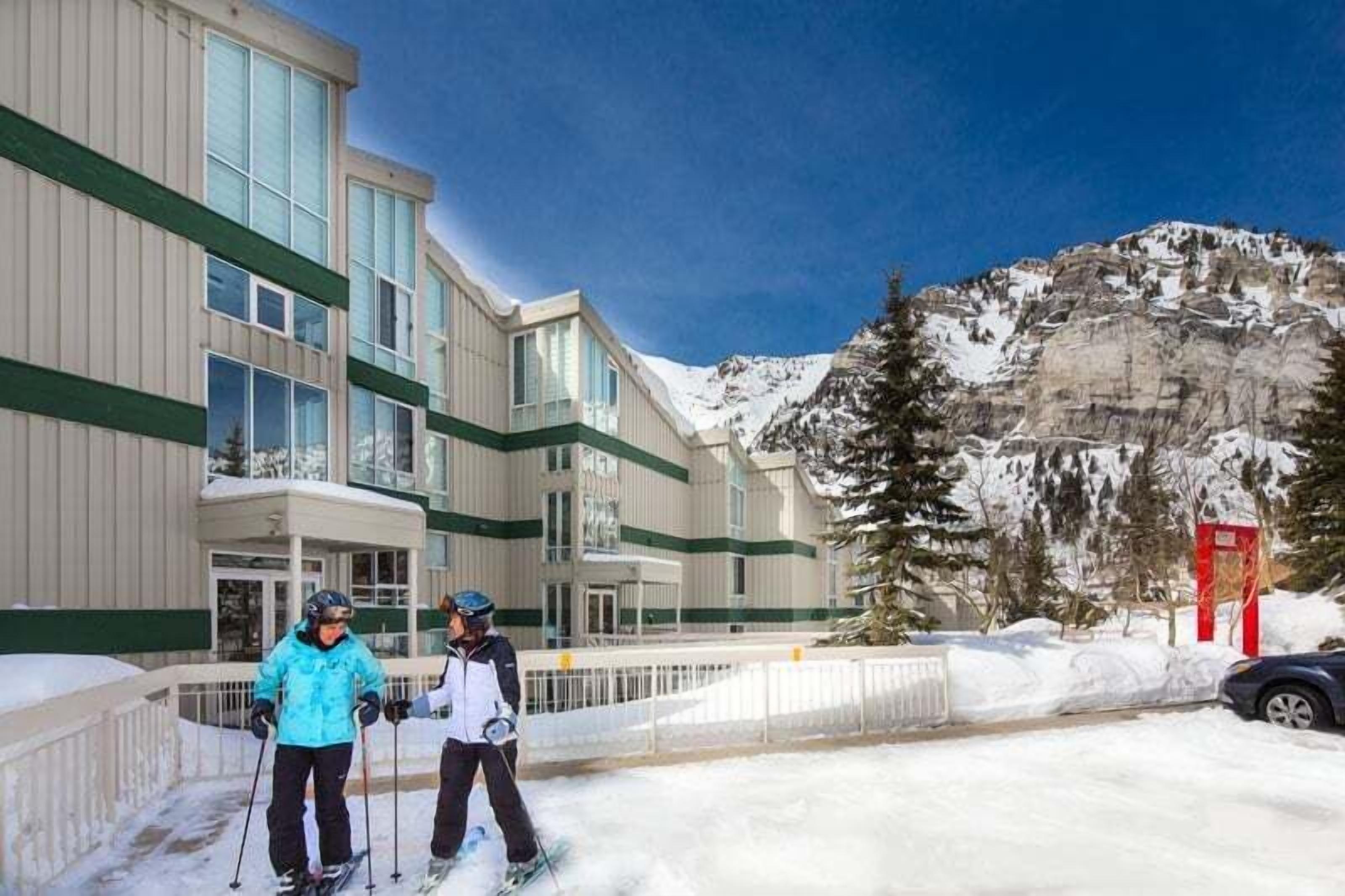 A ski resort building with multiple floors and large windows, surrounded by snow-covered mountains and trees.