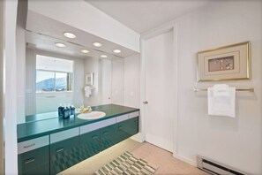 A modern bathroom with a glass vanity, a white sink, and a large mirror. There are recessed ceiling lights, a towel rack, and a framed picture on the wall. - Snowbird Ski in/Ski Out in Quaint Condominium with Fireplace and Mountain View (Alta)