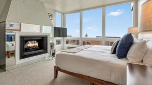 A bedroom with a fireplace, a large bed, a TV, and a view of the city. - Ski in/Ski Out to Snowbird Ski Area in Spacious Condominium with Two Fireplaces (Alta)