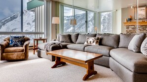 A modern living room with a large sectional sofa, a wooden coffee table, and a dog resting on the sofa. - Ski in/Ski Out to Snowbird Ski Area in Spacious Condominium with Two Fireplaces (Alta)
