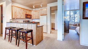A modern kitchen with wooden cabinets, a central island with stools, a refrigerator, and a microwave. - Ski in/Ski Out to Snowbird Ski Area in Spacious Condominium with Two Fireplaces (Alta)