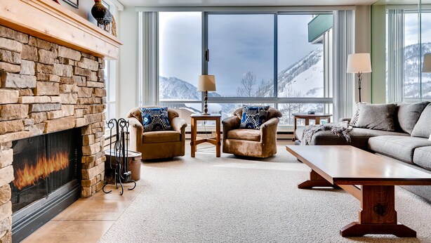 A cozy living room with a stone fireplace, leather armchairs, a wooden coffee table, and a large window offering a mountain view. - Ski in/Ski Out to Snowbird Ski Area in Spacious Condominium with Two Fireplaces (Alta)