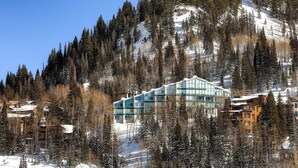 A modern hotel with a glass facade, surrounded by snow-covered trees and a mountain backdrop. - Ski in/Ski Out to Snowbird Ski Area in Spacious Condominium with Two Fireplaces (Alta)
