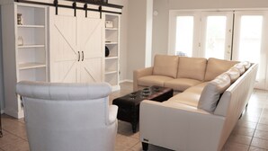Un salon avec un canapé blanc, un fauteuil gris clair, une table basse en bois et un meuble blanc avec des étagères.