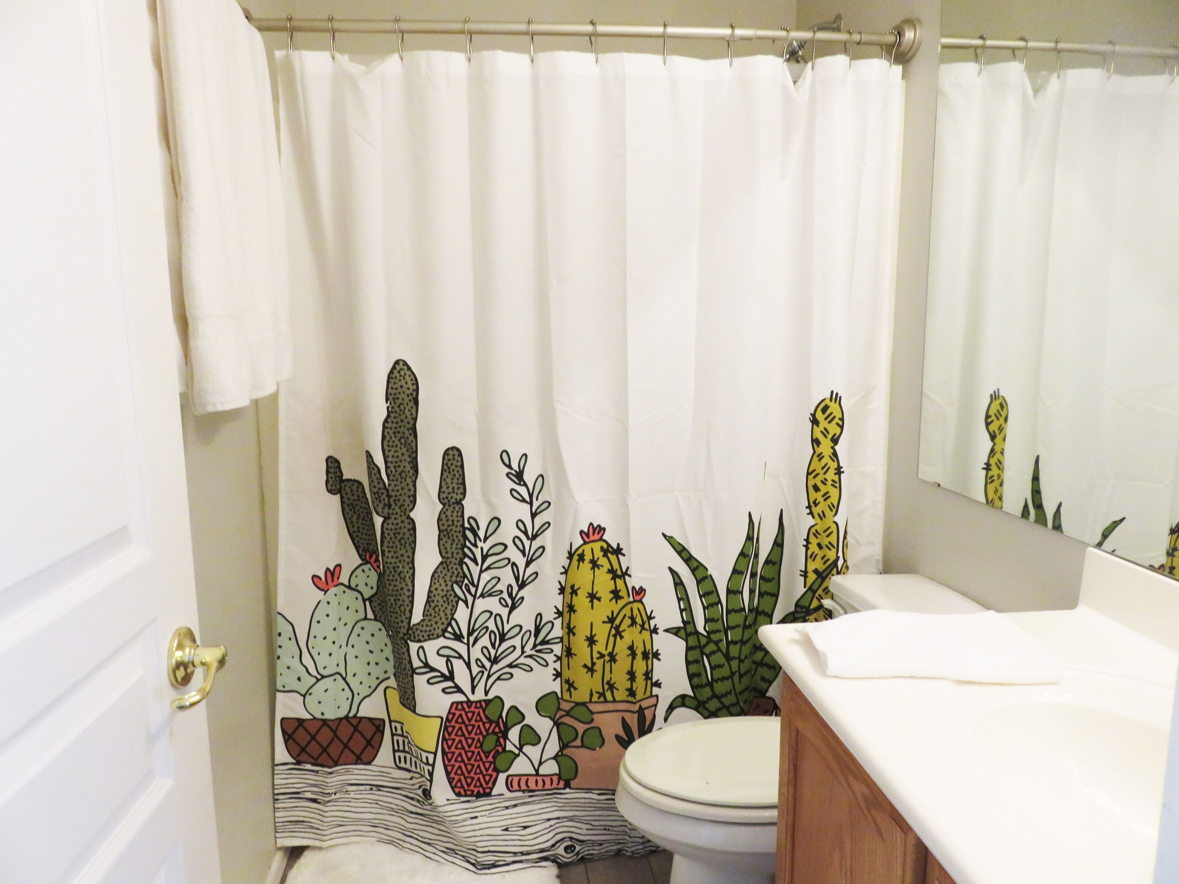 A bathroom with a shower curtain featuring cactus and succulent designs, a toilet, and a sink with a mirror above it.