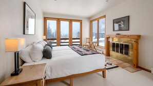 A bedroom with a large bed, a fireplace, and a view of a snowy landscape through large windows. - Luxury Alta Utah Home with Hot Tub, Pool Table, Game Room and Chef's Kitchen (Alta)