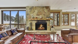 A cozy living room with a stone fireplace, leather sofas, and a large window overlooking a snowy mountain. - Luxury Alta Utah Home with Hot Tub, Pool Table, Game Room and Chef's Kitchen (Alta)