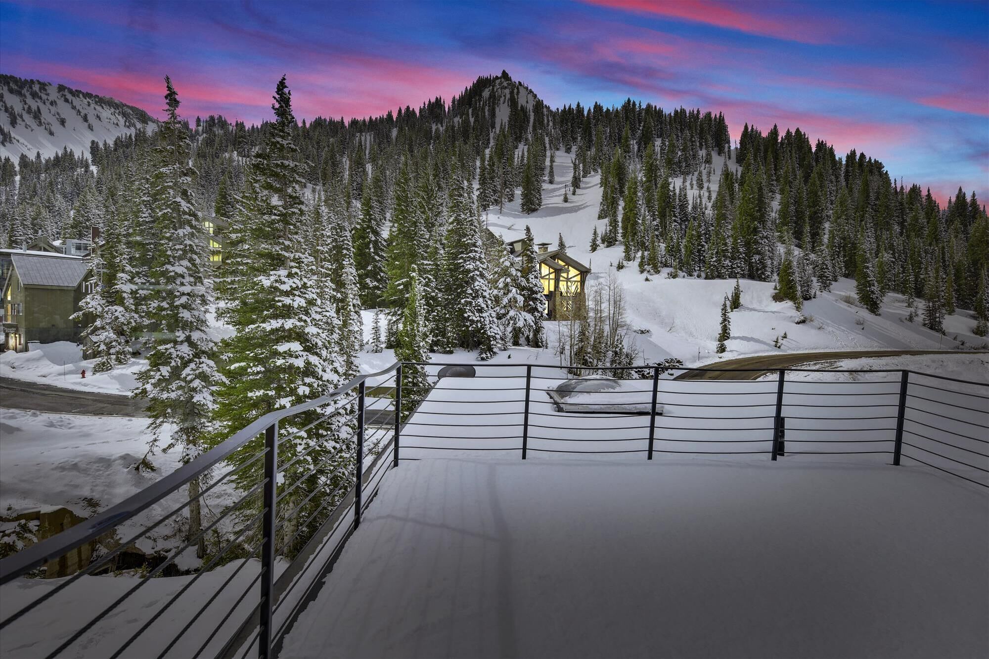 A snow-covered ski resort with a mountain backdrop, a wooden lodge, and a snow-covered deck with railings.