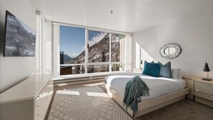 A bedroom with a large window, a bed with blue pillows, a bedside table, and a mirror on the wall. - Ski in/Ski Out to Snowbird in this Delightful Condominium with Fireplace (Alta)