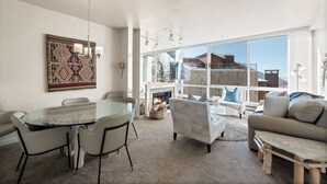 A spacious living area with a glass dining table, comfortable seating, a fireplace, and large windows offering a view of the outdoors. - Ski in/Ski Out to Snowbird in this Delightful Condominium with Fireplace (Alta)