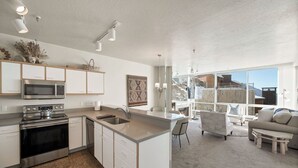 A modern kitchen with a central island, stainless steel appliances, and a large window overlooking a snowy landscape. - Ski in/Ski Out to Snowbird in this Delightful Condominium with Fireplace (Alta)