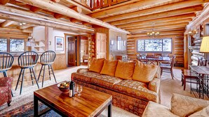 Ein Blockhaushaus-Interieur mit Holzbalkendecke, einer Couch mit gemusterten Kissen, einem Esstisch und Stühlen.