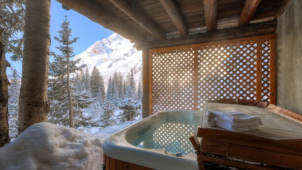Eine Holzhütte mit Whirlpool, Holzfassade und Blick auf verschneite Berge.