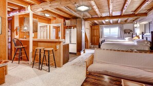 Ein gemütliches Blockhausszimmer mit Holzbalkendecke, einer Küchenzeile, einem Essbereich und zwei Betten.