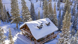 Eine Holzhütte mit verschneitem Dach, umgeben von hohen Kiefern.