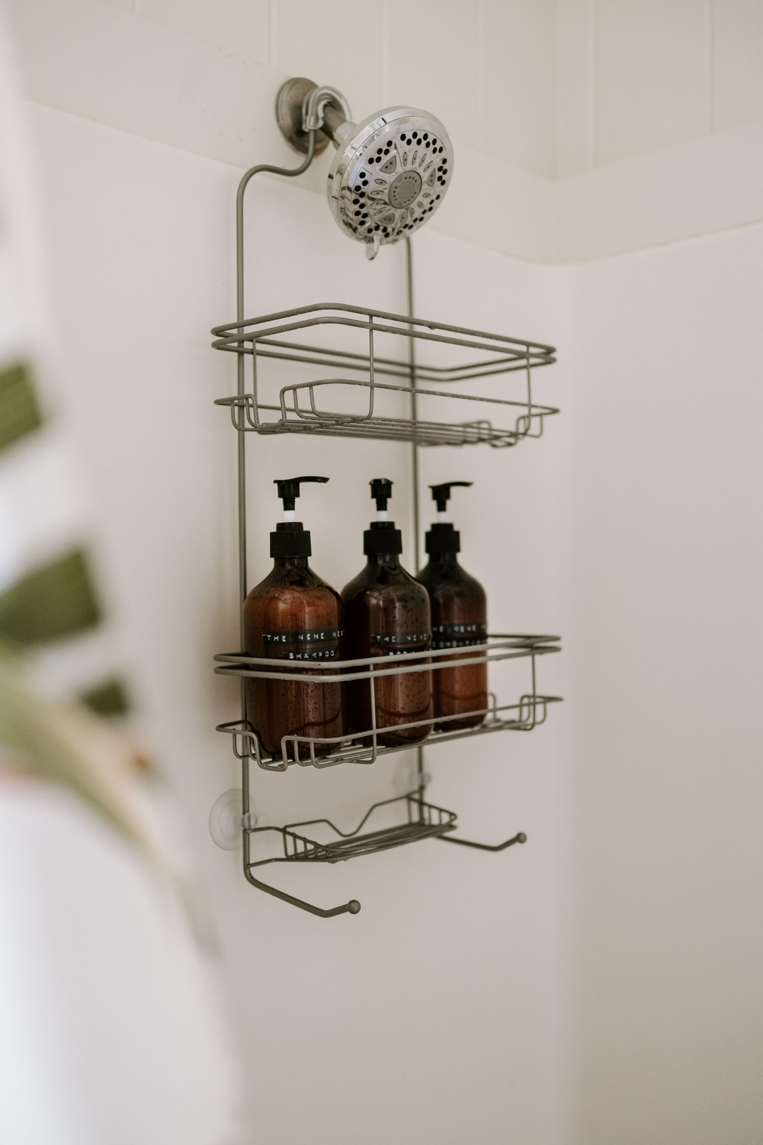 A bathroom with a wall-mounted shower and a metal shelf holding three bottles of shampoo.