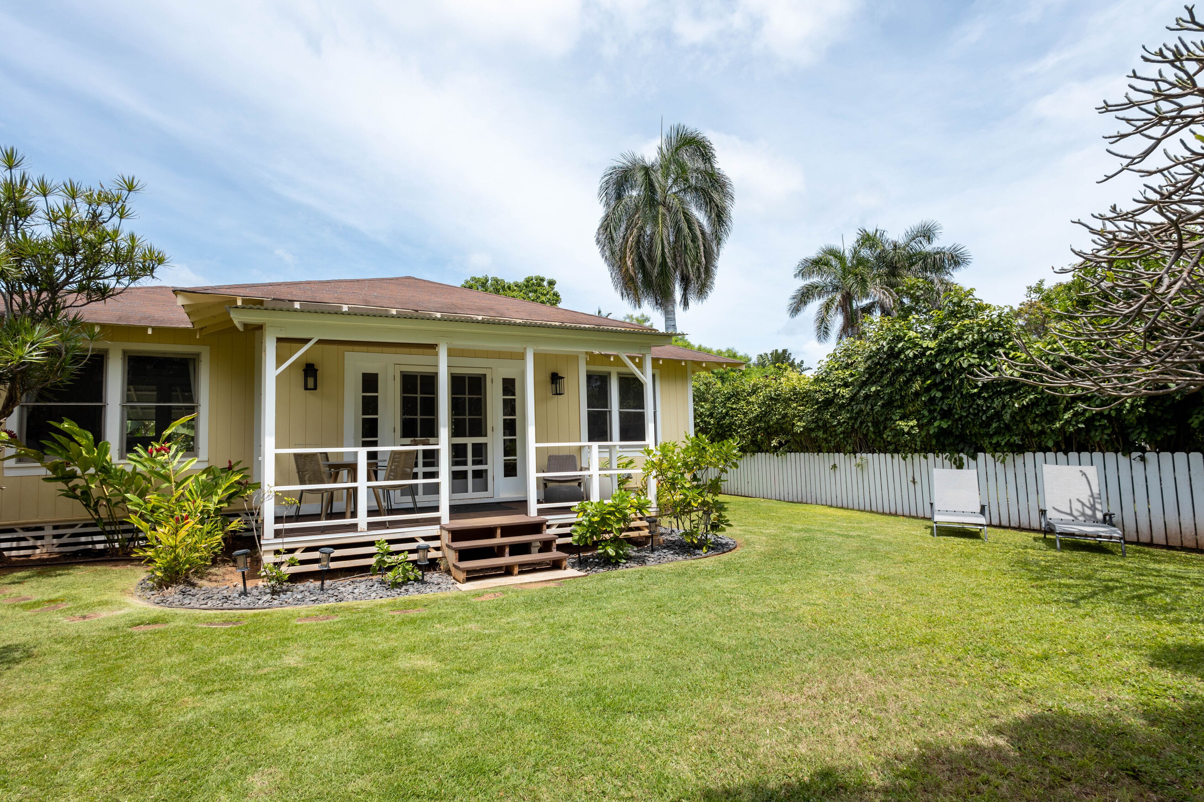 A single-story house with a porch, surrounded by a well-maintained lawn and a wooden fence.
