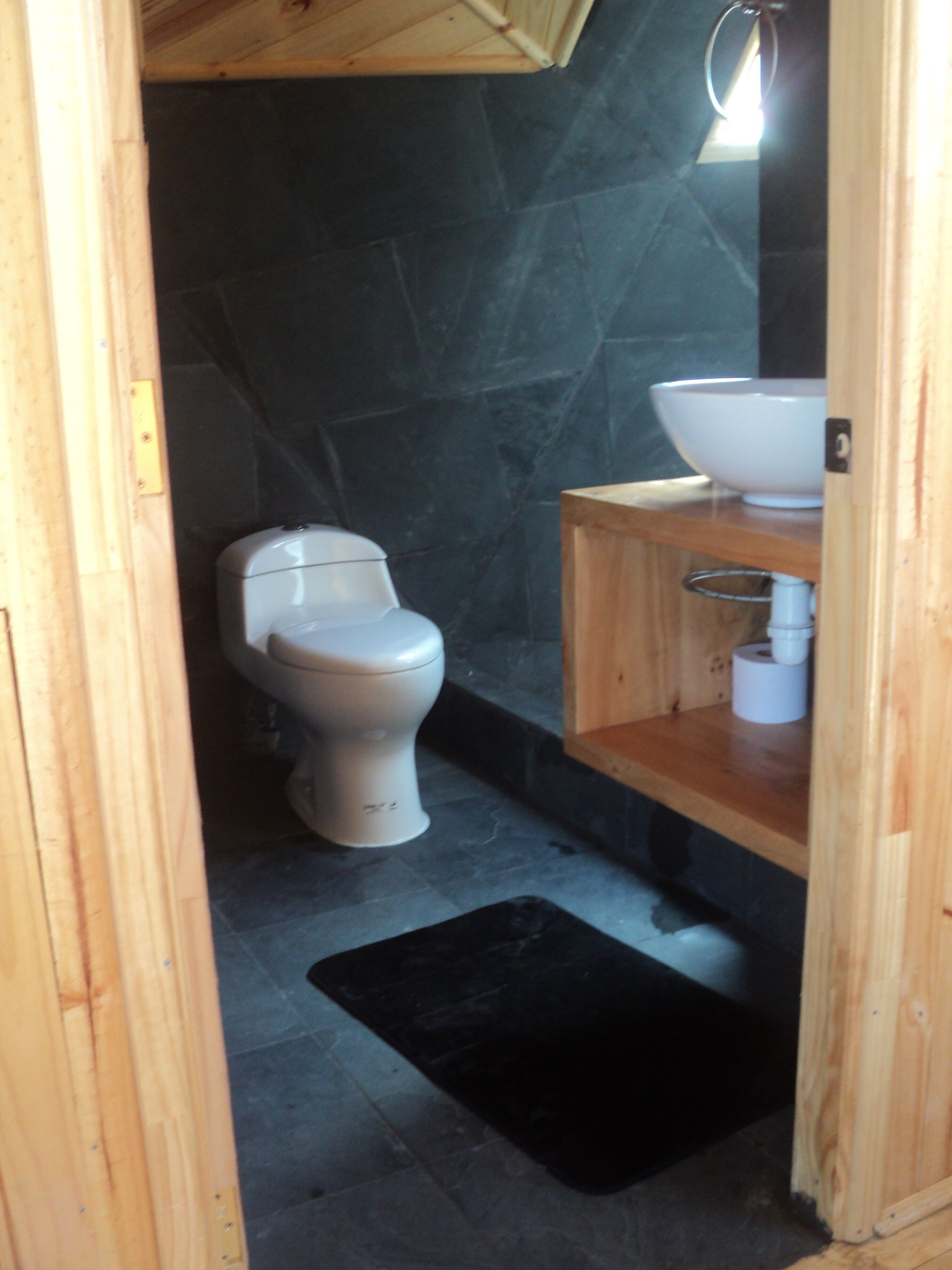 A small, compact bathroom with a toilet, a wooden vanity with a sink, and a black mat on the floor.