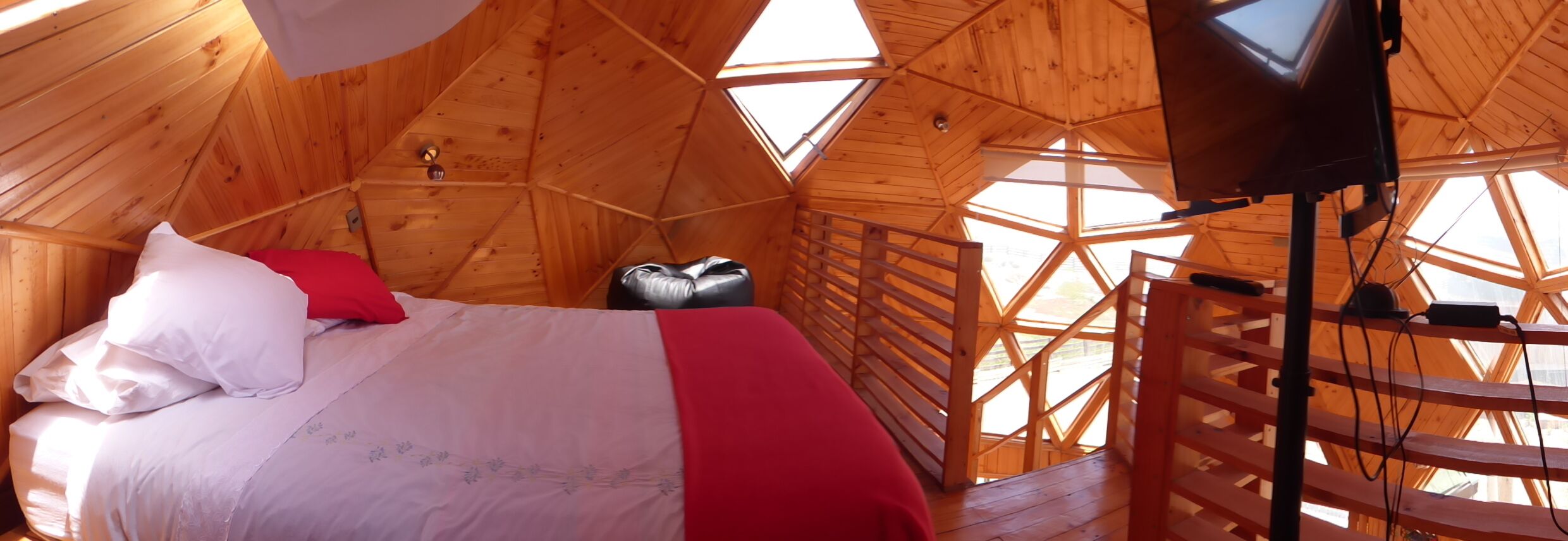 A wooden cabin with a bed, a small stool, and a TV mounted on the wall.