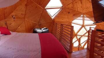 A wooden cabin with a bed, a small stool, and a TV mounted on the wall.