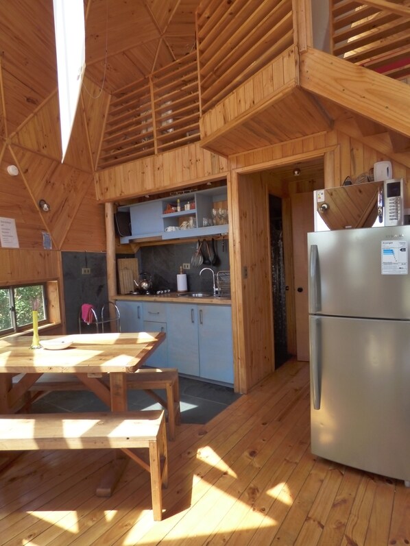 A wooden cabin interior with a kitchen area, a dining table, and a refrigerator. - Dune & Domes Pichilemu (Pichilemu)