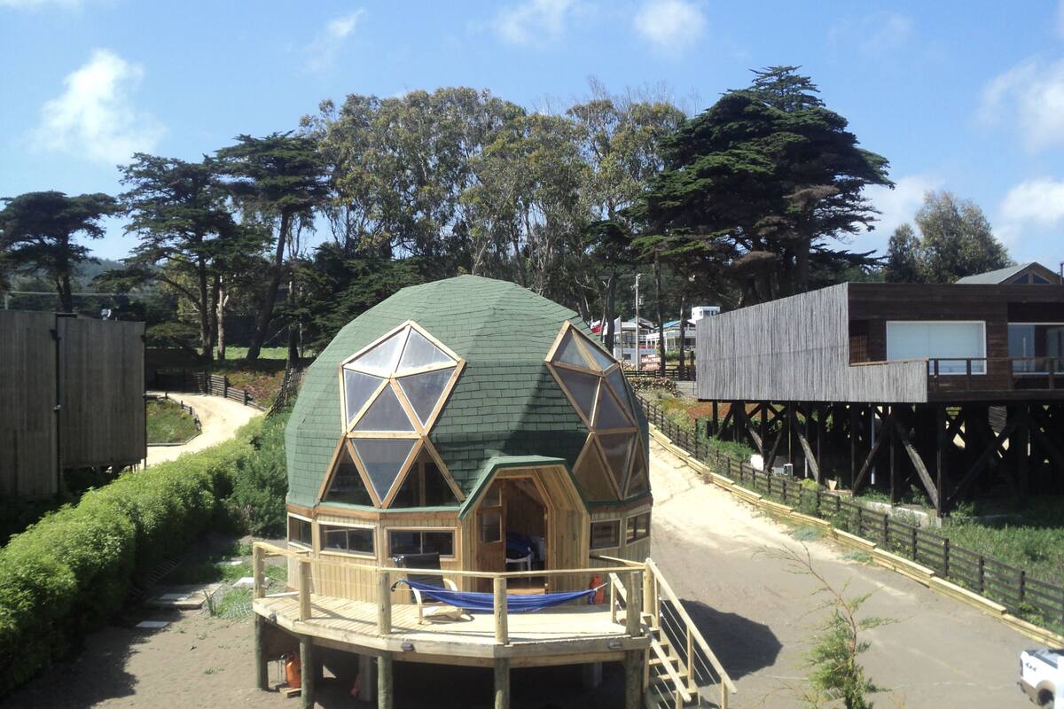 Une structure en forme de dôme géodésique, dotée d’une terrasse en bois et d’une seule fenêtre.