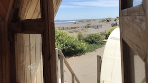 Een houten strandhuis met uitzicht op de oceaan en een surfplank op het terras.