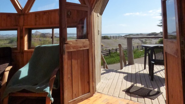 Een houten blokhut met een terras, een stoel en uitzicht op het strand.