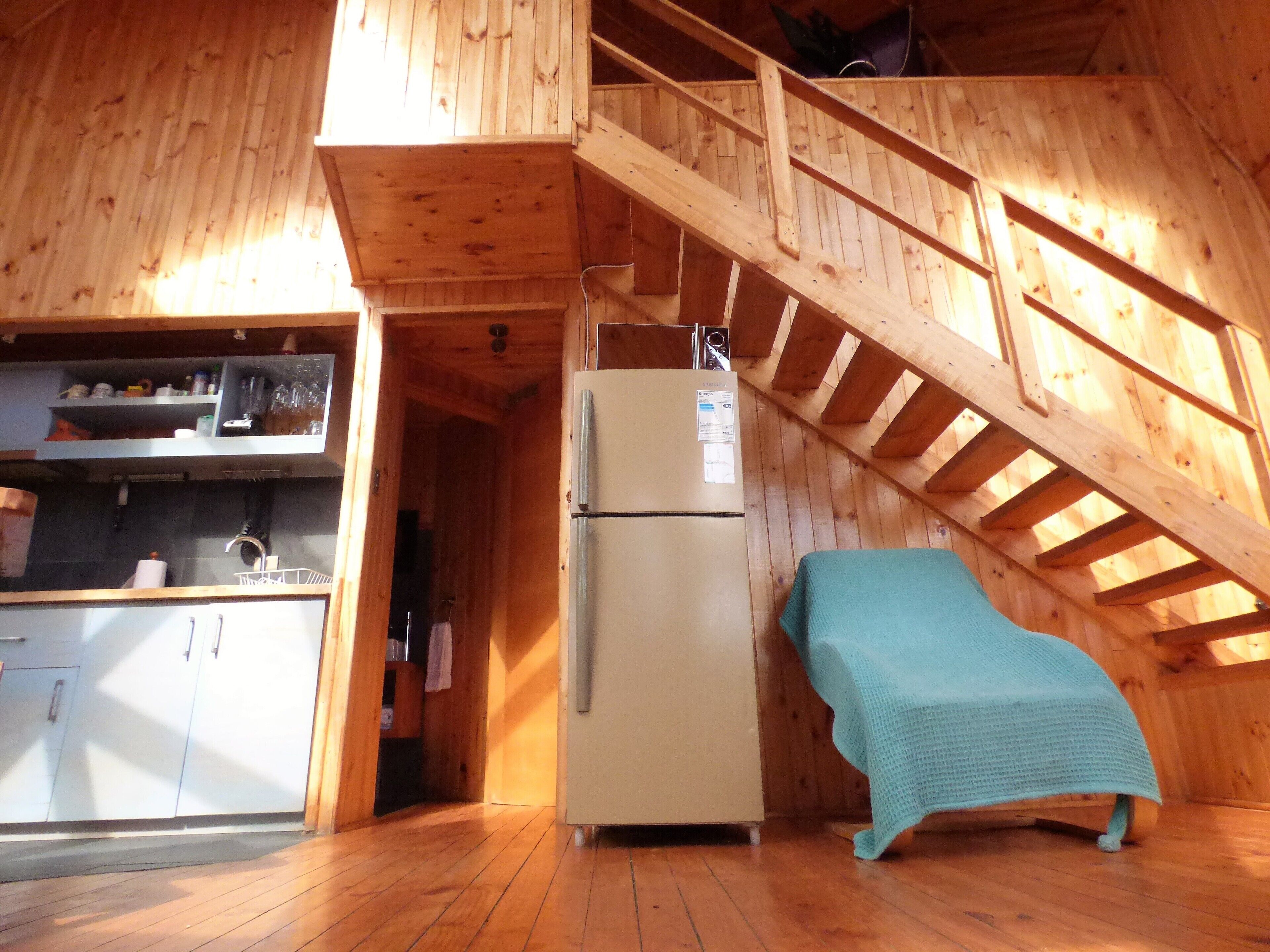 A wooden cabin with a kitchen area, a refrigerator, and a bunk bed.