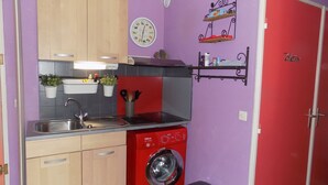A compact kitchen with a washing machine, a sink, and wooden cabinets. - Charming, colourful and functional T2 apartment 200m from the beach free, enclosed parking (Sète)