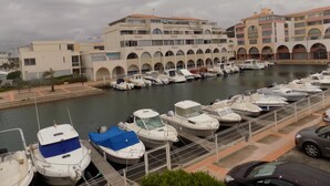 A marina with several boats docked, a building with arched windows, and a car parked nearby. - Charming, colourful and functional T2 apartment 200m from the beach free, enclosed parking (Sète)