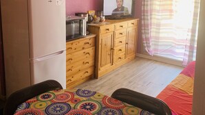 A bedroom with a bed, a wooden dresser, a refrigerator, a television, and a window with curtains. - Charming, colourful and functional T2 apartment 200m from the beach free, enclosed parking (Sète)