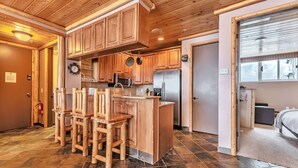 A kitchen with wooden cabinets, a stainless steel refrigerator, and a bar area with stools. - Updated Condominium with Fireplace, Wine Fridge and Granite Countertops (Alta)