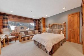 A cozy log cabin bedroom with a large bed, a wooden headboard, a sofa, and a chair.