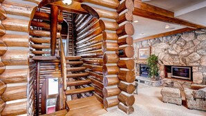 A log cabin interior with a spiral staircase, stone fireplace, and a television mounted on the wall. - Luxury and Location in this Incredible Home with Brand New Outdoor Hot Tub and 2 Car Garage! (Alta)