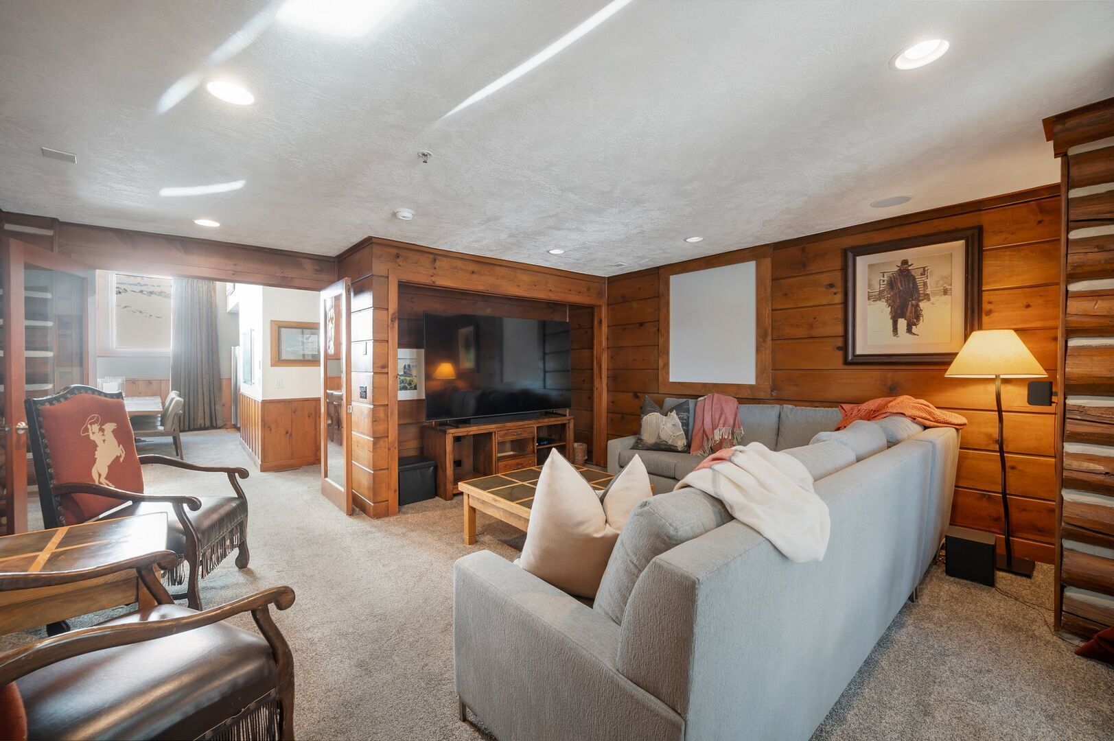 A cozy log cabin interior with a sofa, a television, and a dining area.