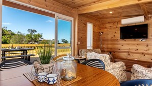A wooden interior with a dining table, chairs, a TV, and a view of the outdoors.
