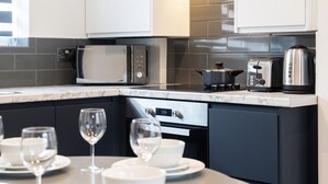 Una cocina moderna con armarios blancos, microondas, tostadora y hervidor. Hay una mesa de comedor lista con platos, tazones y copas de vino.