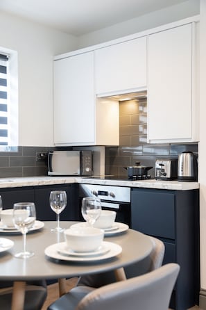 A modern kitchen with white cabinets, a microwave, a toaster, and a kettle. There is a dining table set with plates, bowls, and wine glasses.