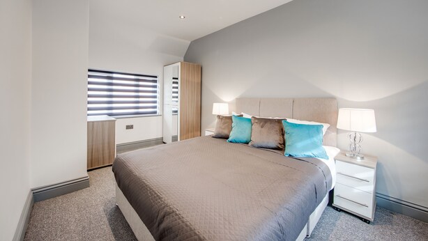 Un dormitorio moderno con una cama grande, una mesita de noche, un armario y una ventana con persianas.