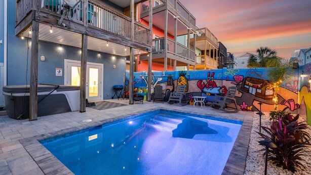 A multi-story building with a swimming pool, outdoor seating, and a colorful mural. - Beach Side “Crabby Paddy", Luxury family retreat 6br 4+ bath w pool+hot tub (Panama City Beach)