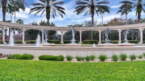 Une fontaine dotée de plusieurs jets d’eau et ornée de sculptures, entourée de palmiers et d’une pelouse bien entretenue.