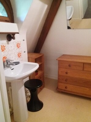 Une salle de bain avec un lavabo blanc, des toilettes noires, un meuble en bois et une fenêtre avec une poutre en bois.