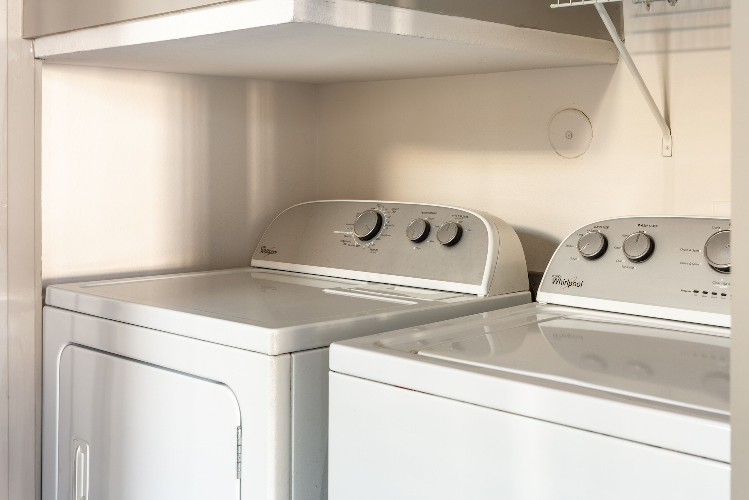 Een wasruimte met twee gestapelde wasmachines en drogers, een roestvrijstalen afzuigkap erboven, en een witte muur.