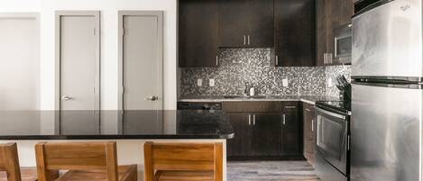 A modern kitchen with dark cabinets, a stainless steel refrigerator, and a black countertop.