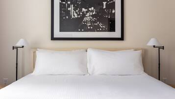 A neatly made bed with white linens, a framed cityscape photo above it, and two bedside lamps on either side.