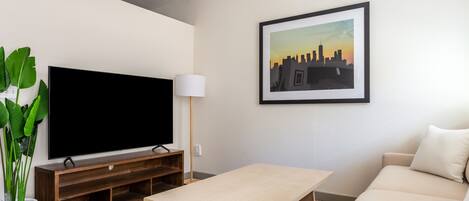 Una sala de estar moderna con televisor de pantalla plana, una mesa de centro, un sofá, un cuadro enmarcado con una vista urbana y una planta en maceta.