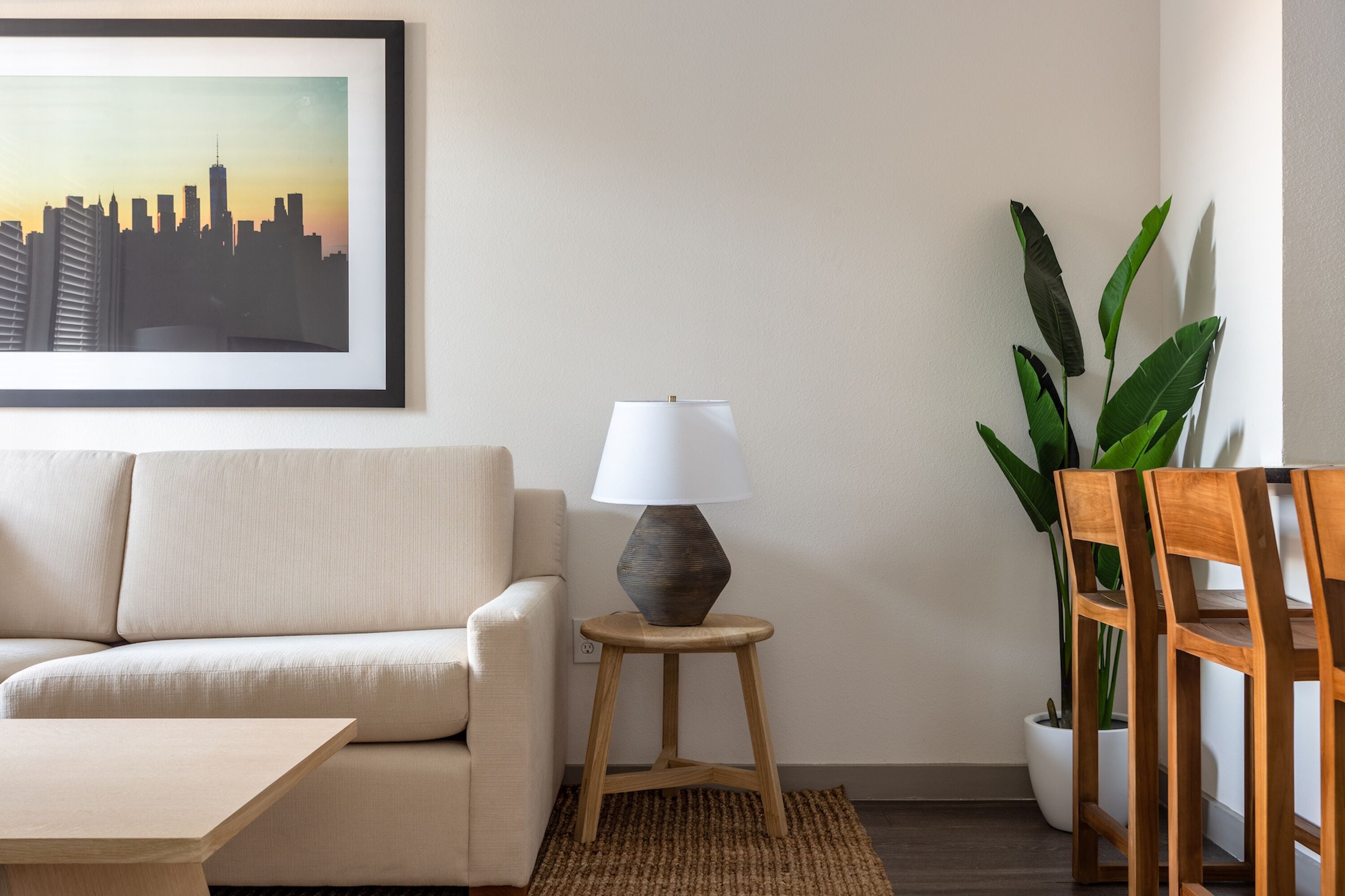 A living room with a sofa, a lamp on a stool, a potted plant, and a framed picture on the wall.